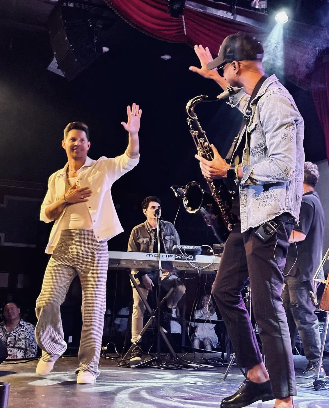 Luiso plays saxophone next to Leoni Torres, who raises a hand to greet him during a concert.
