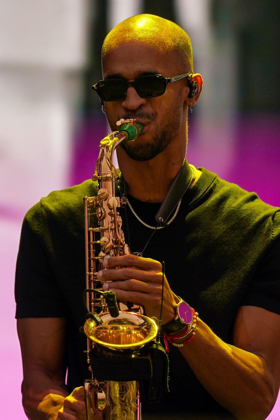 Close-up of Luiso on alto saxophone, between yellow and pink lights.