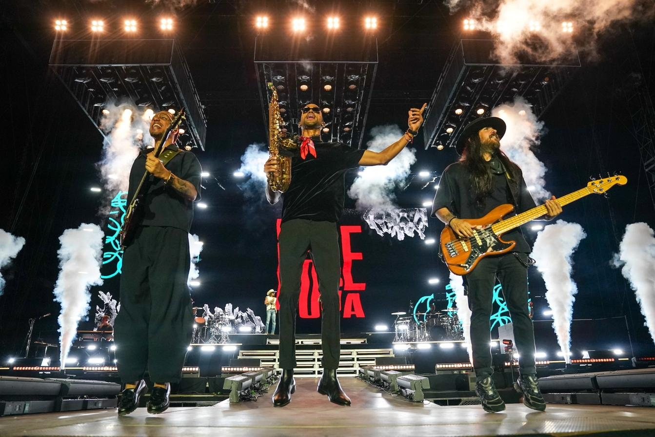 Luiso jumping on stage with his saxophone raised, among jets of smoke and lights, alongside the band.